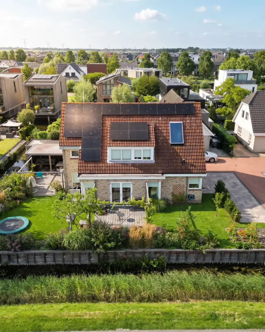 Woning met een dak vol zwarte zonnepanelen in de zon, gezien vanuit de lucht